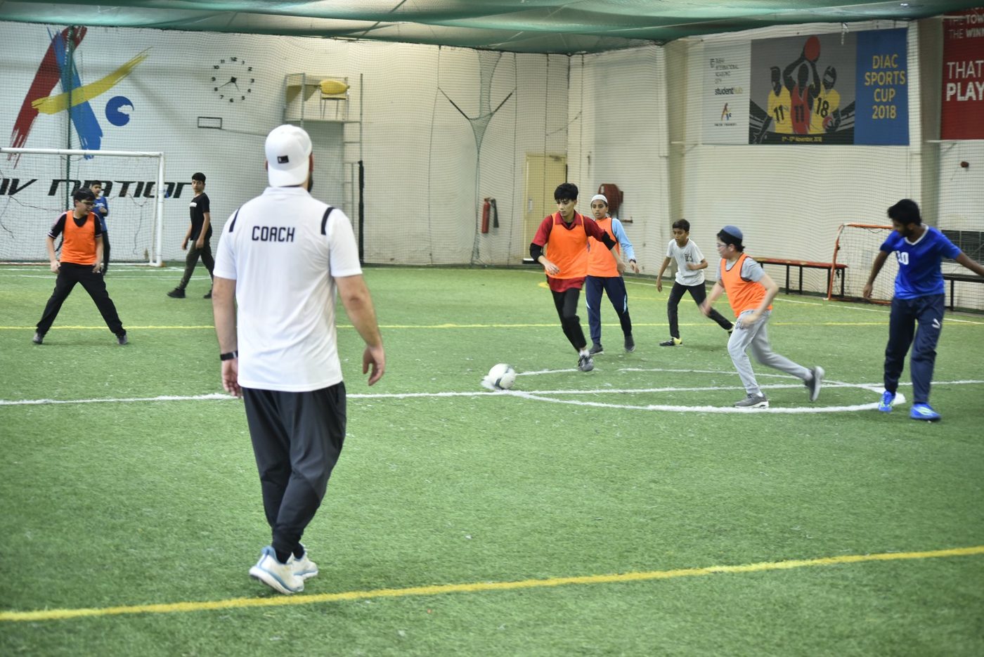 Coach watching students play football in an indoor arena