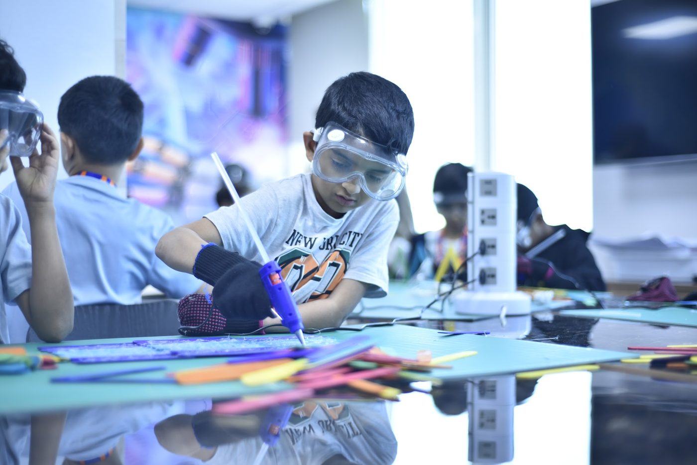 Student in safety goggles building a project with a glue gun in the STEM Lab