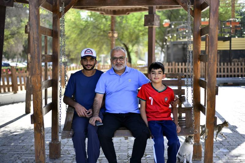 Father seated on the swing between his two sons with a cat beside them