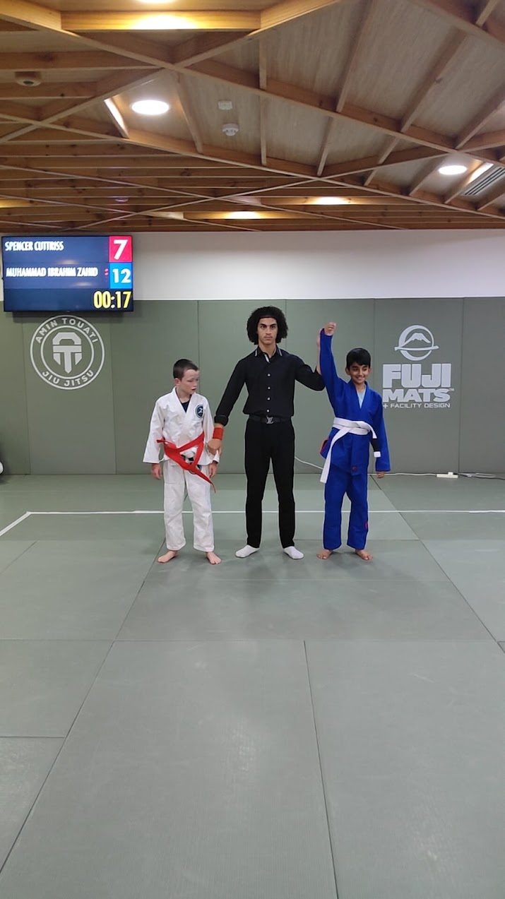 Referee raising the winning competitor's hand with the scoreboard behind them