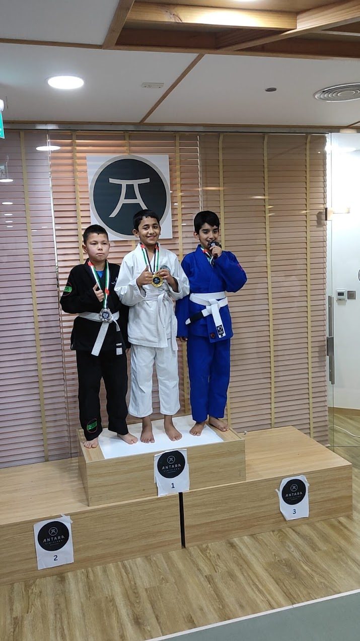 Three competitors in gis standing on the official tournament podium with their medals