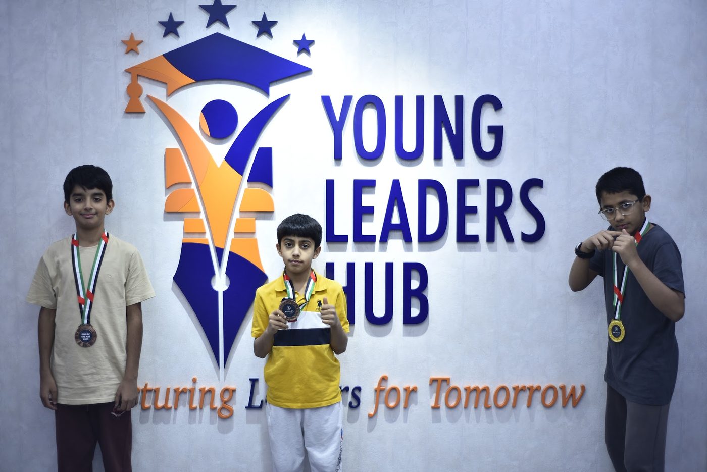 Three medalists posing in front of the Young Leaders Hub sign