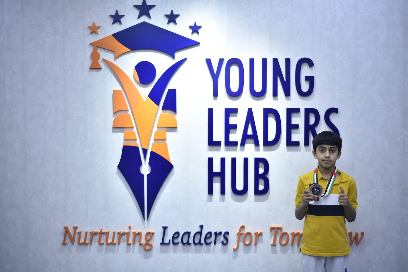 Medal winner posing with his bronze medal in front of the Young Leaders Hub sign