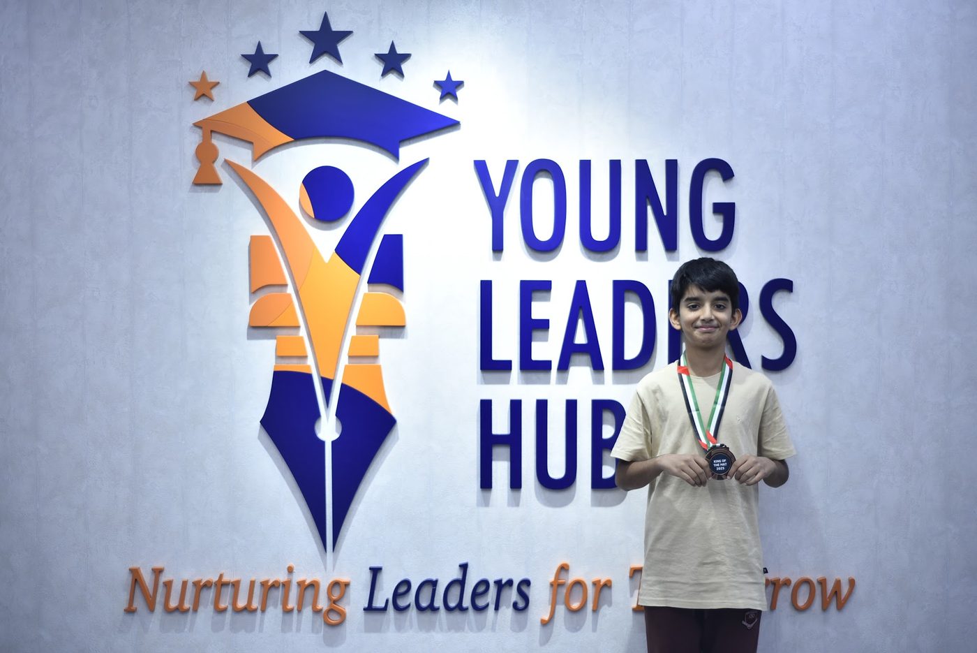 Medal winner posing with his bronze medal in front of the Young Leaders Hub sign