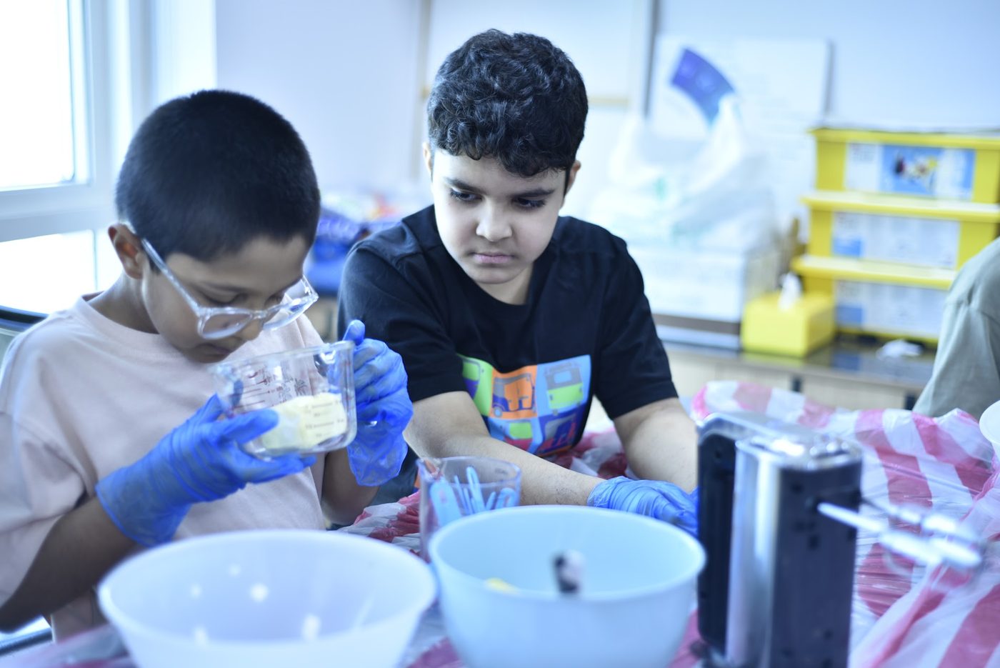 Students in gloves and safety glasses measuring and mixing ingredients in a hands-on life skills activity