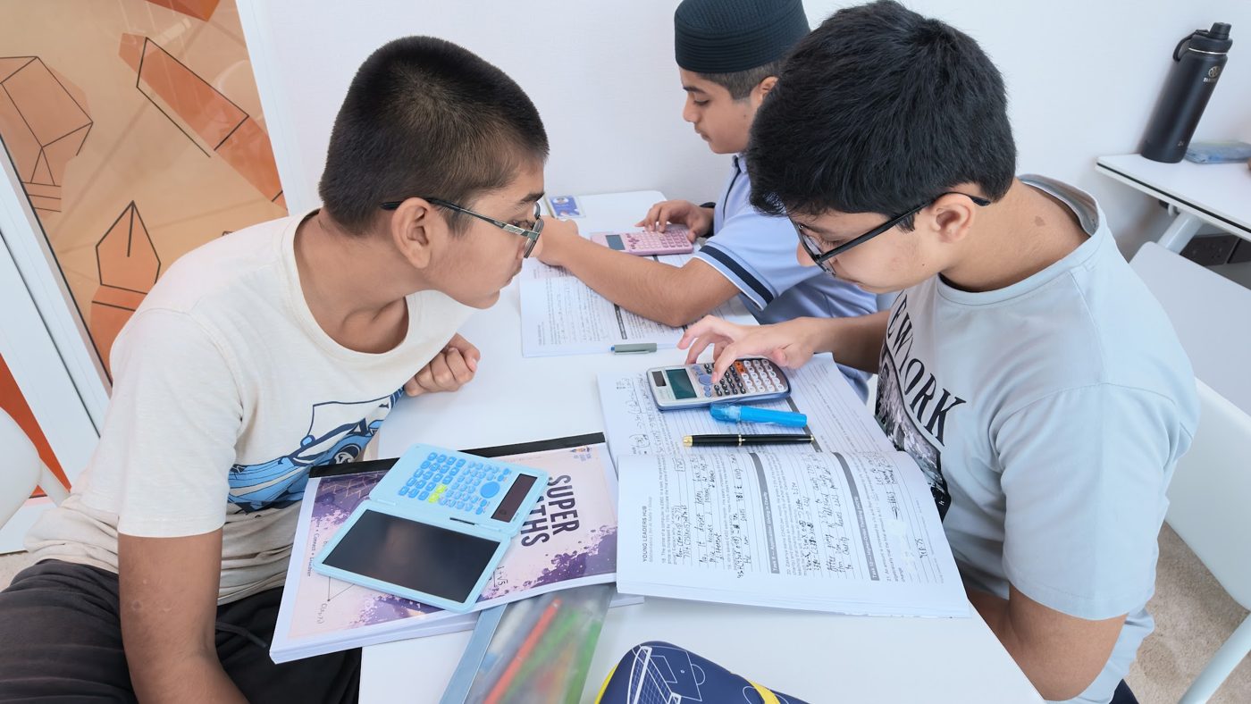 Students solving Super Maths workbook problems with calculators
